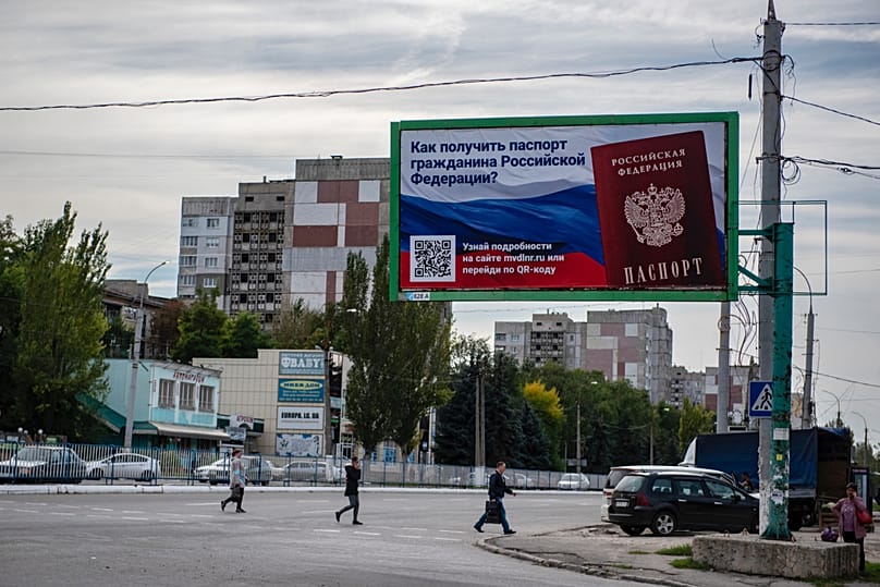 FILE: People cross a street with a billboard reading "How to get a passport of a citizen of Russia" in Luhansk, Ukraine, Sept. 22, 2022.
