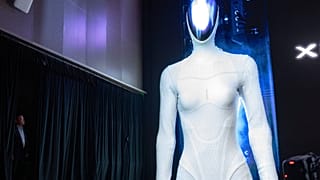 He Xiaopeng, presidente e CEO da XPENG, espreita por detrás de uma cortina enquanto a imagem do robô IRON de nova geração da empresa surge no ecrã durante o XPENG AI Day