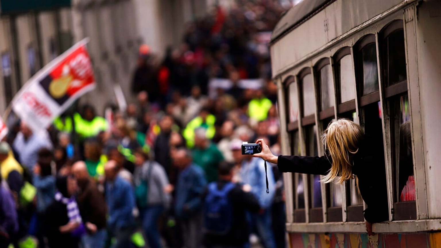 ARQUIVO (25.11.2014): Uma mulher tira fotografias de dentro de um elétrico enquanto as pessoas marcham durante um protesto da CGTP em Lisboa
