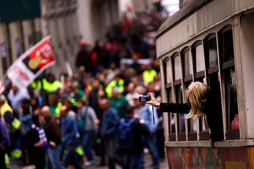 ARQUIVO (25.11.2014). Uma mulher tira fotografias de dentro de um elétrico enquanto as pessoas marcham durante um protesto organizado pela principal confederação sindical
