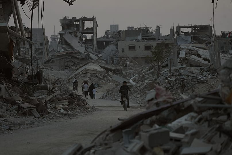 Displaced Palestinians walk among the ruins of destroyed buildings in Khan Younis, Gaza Strip, Saturday, 8 November 2025.