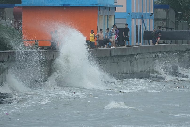 People stand as strong waves due to Typhoon Fung-wong hit the seawall along a coastal village on Monday, Nov. 10, 2025, in Navotas, Philippines.