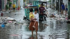 Eine Frau und ein Kind überqueren eine überflutete Straße in Navotas auf den Philippinen. Taifun Fung-wong und Flut am zehnten November 2025. (AP Photo/Aaron Favila)