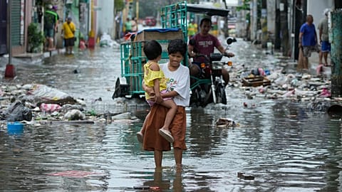 Une femme et un enfant traversent une rue inondée à cause du typhon Fung-wong et de la marée haute, lundi 10 novembre 2025, à Navotas, aux Philippines. (Photo AP/Aaron Favila)