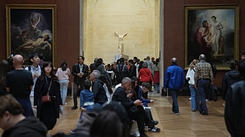 The marble hellenic sculpture The Winged Victory of Samothrace, center, is pictured as people visit the Louvre museum three days after historic jewels were stolen.