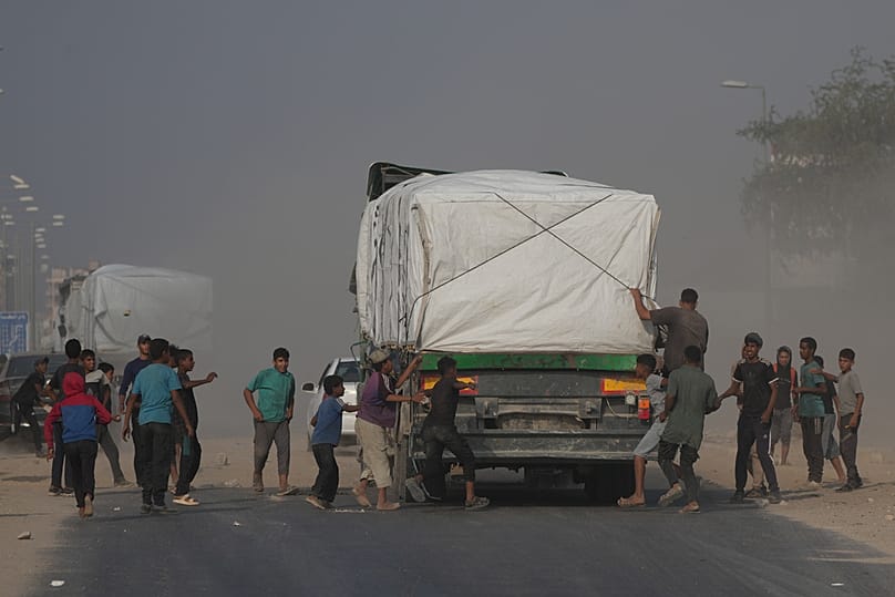 فلسطينيون يسارعون نحو الشاحنات التي تحمل المساعدات أثناء مرورها عبر دير البلح في وسط غزة، الأحد 9 نوفمبر/تشرين الثاني 2025.
