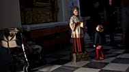 Un niño mira a una figura que representa a un monaguillo pidiendo donaciones dentro de una iglesia en Medina Sidonia, Cádiz, España, el 29 de marzo de 2013.