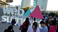 Attendees pose for pictures by the logo of the Web Summit technology conference outside its venue, in Lisbon, Monday, Nov. 13, 2023. 