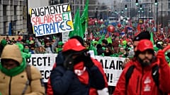 Συνδικαλιστές διαδηλώνουν με μια πινακίδα που γράφει "αύξηση μισθών και συντάξεων" κατά τη διάρκεια διαδήλωσης στις Βρυξέλλες, 16 Δεκεμβρίου 2022. 