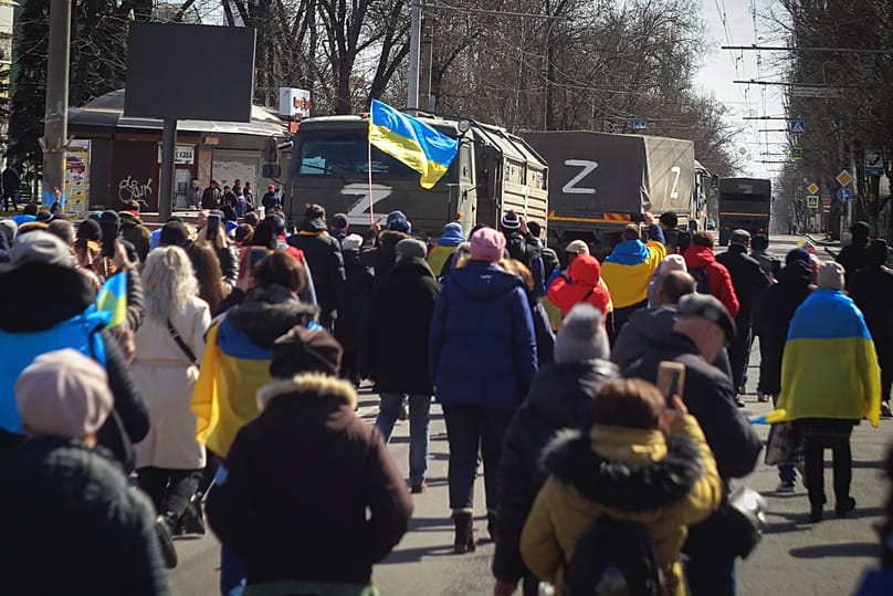 DOSSIER - Des personnes portant des drapeaux ukrainiens se dirigent vers des camions de l'armée russe lors d'un rassemblement contre l'occupation russe à Kherson, en Ukraine, le 20 mars 2022.