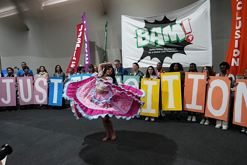 A performer participates in a demonstration near a sign that reads "just transition" a protest for the transition away from fossil fuels at the COP30 U.N. Climate Summit.