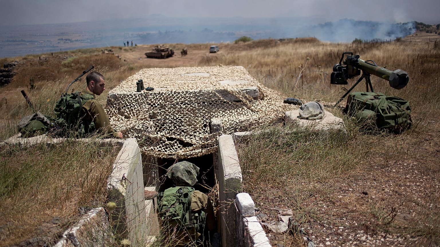 يجلس جنود إسرائيليون في موقع على الحدود مع سوريا في هضبة الجولان التي تسيطر عليها إسرائيل، بينما يرتفع الدخان عقب انفجارات، يوم الثلاثاء، 16 يوليو 2013.