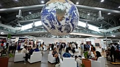 Participantes sentam-se sob um globo num átrio dos pavilhões de eventos paralelos da Cimeira do Clima da ONU COP30