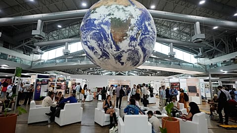 Attendees sit under a globe in a lobby at the side events pavilions at the COP30 UN Climate Summit,
