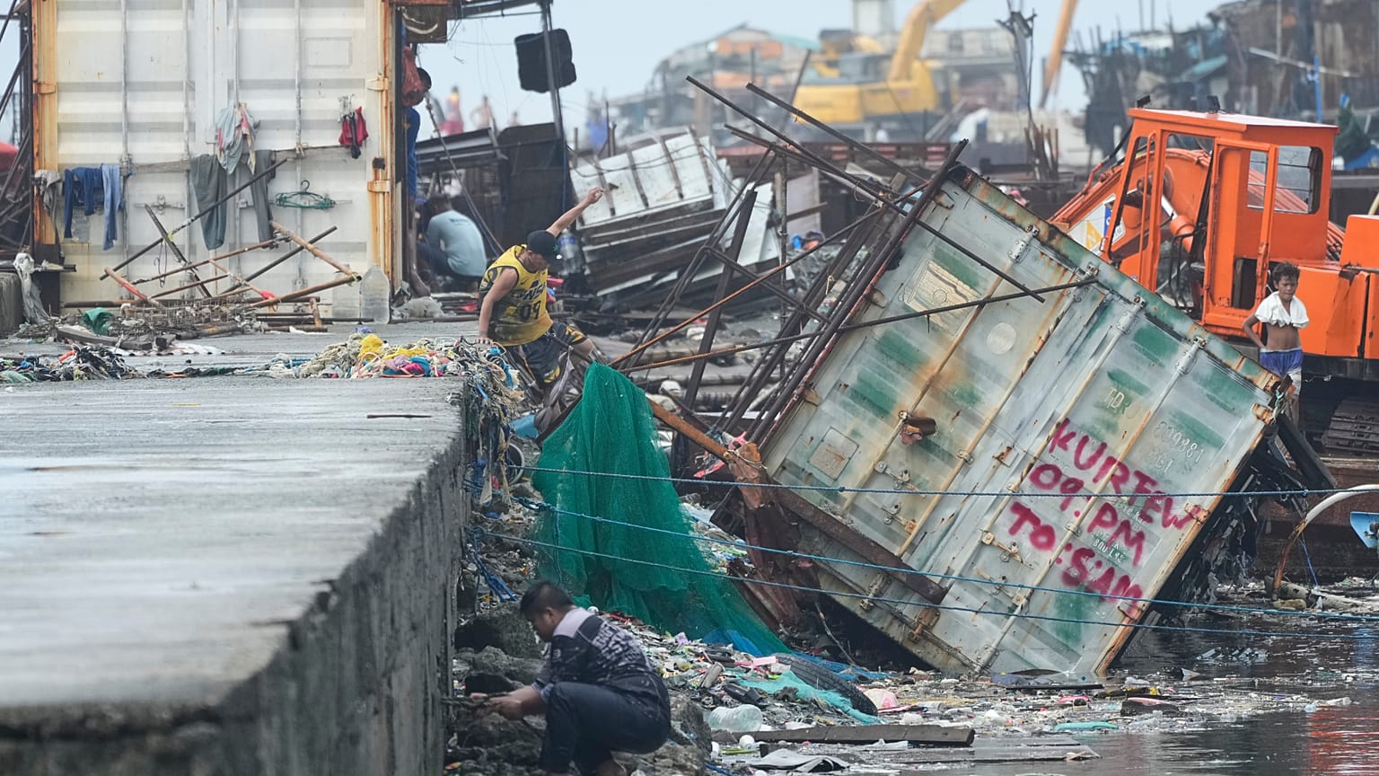 Un homme saute à côté d'un conteneur renversé par le typhon Fung-wong, le lundi 10 novembre 2025, à Navotas, aux Philippines