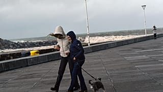 Mujeres pasean con un perro bajo un fuerte viento en la ciudad de San Sebastián, norte de España, el martes 17 de enero de 2023.