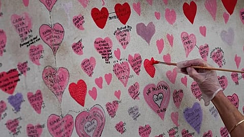 A volunteer re-paints a faded heart on the COVID-19 memorial wall in London, 15 October, 2021