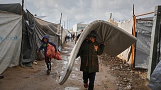 يسير فلسطيني بين الخيام بعد هطول الأمطار في مخيم مؤقت بمدينة دير البلح وسط قطاع غزة، يوم الجمعة 14 نوفمبر 2025.