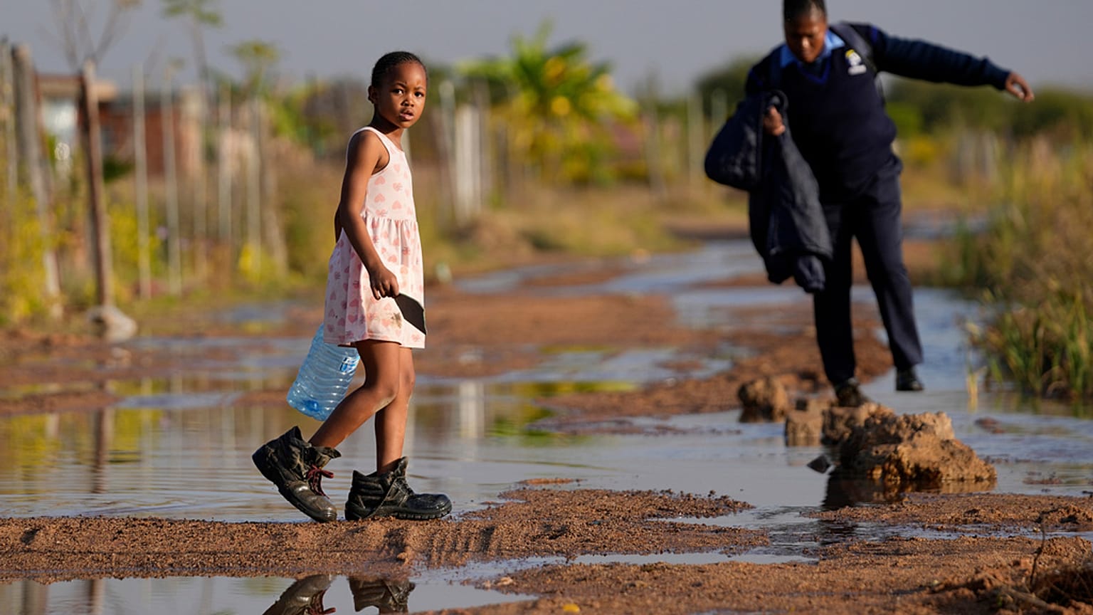 A young girl carrying an empty water bottle through a flooded street caused by an overflowing water reservoir in Hammanskraal, Pretoria, South Africa, 26 May, 2023