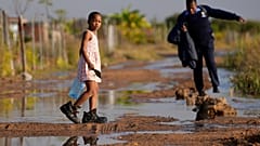 Ein junges Mädchen trägt eine leere Wasserflasche durch eine überflutete Straße. Ein Wasserreservoir lief über. Hammanskraal, Pretoria, Südafrika, 26. Mai 2023.