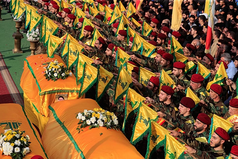  يرفع مقاتلو حزب الله أعلام جماعتهم أثناء وقوفهم بجانب نعوش خمسة من رفاقهم، خلال موكب جنازتهم في النبطية في لبنان، الأحد 2 نوفمبر/تشرين الثاني 2025. 