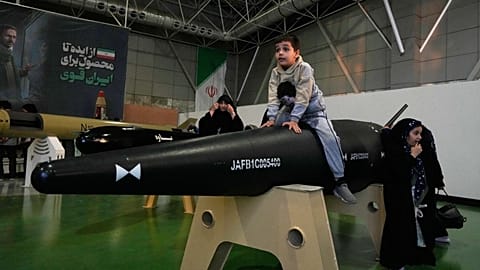 Un garçon est assis sur l’ogive d’un missile iranien de fabrication nationale, exposé lors d’un salon à Téhéran, en Iran, le 13 novembre 2025