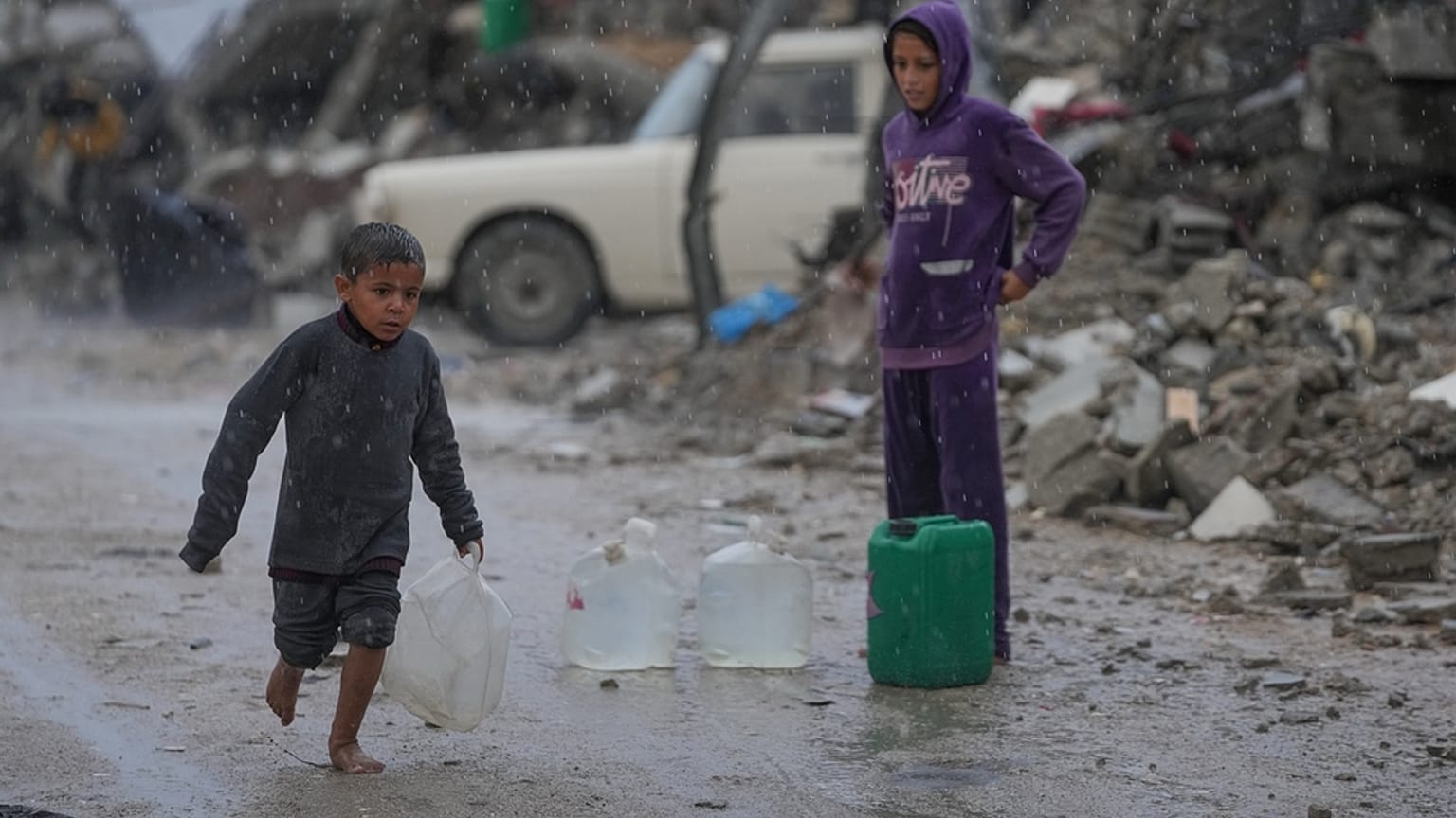 يمشي طفل حافي القدمين تحت المطر حاملاً جالونًا بلاستيكيًا من الماء في حي الشيخ رضوان بمدينة غزة، يوم الجمعة 14 نوفمبر/تشرين الثاني 2025. (صورة من وكالة أسوشيتد برس