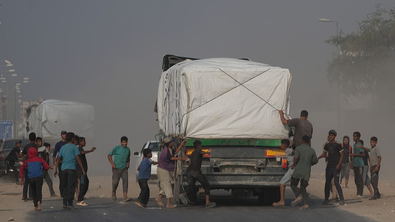  فلسطينيون يهرعون نحو شاحنات المساعدات لدى مرورها في دير البلح وسط غزة، الأحد 9 تشرين الثاني 2025.
