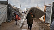 فلسطيني يحمل فراشًا وهو يسير بين الخيام بعد هطول الأمطار في مخيم مؤقت في دير البلح، بوسط قطاع غزة، يوم الجمعة الموافق 14 نوفمبر/تشرين الثاني 2025.