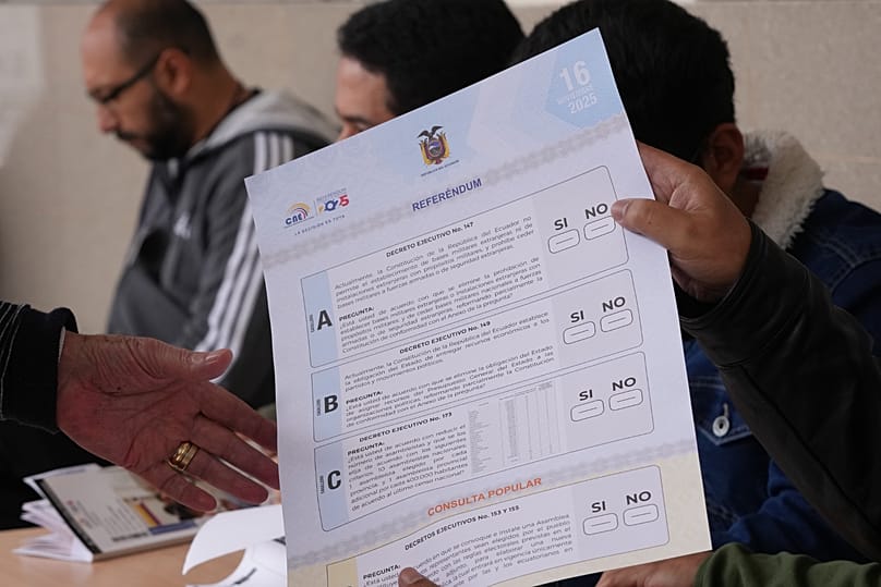 An electoral worker hands a ballot to a voter in a referendum on whether to allow foreign military bases and rewrite the constitution, in Quito, Ecuador, Sunday, Nov. 16, 2025