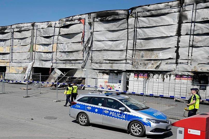 Policjant przechodzi obok tymczasowego ogrodzenia ustawionego, by zablokować dostęp do spalonego centrum handlowego w Warszawie, w środę, 15 maja 2024 r. 