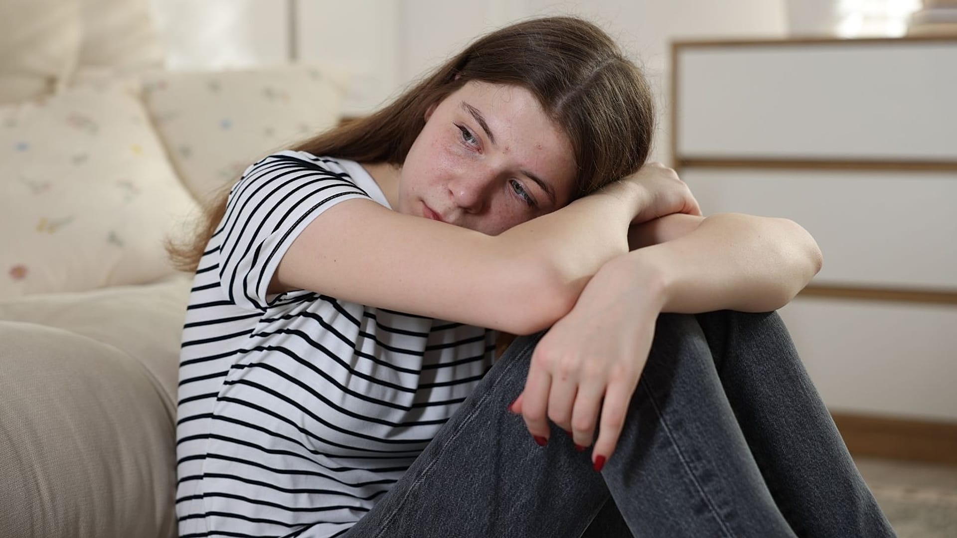 Üzgün bir genç kız kadrajın dışına bakıyor.