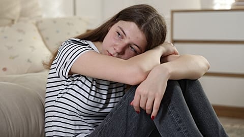 A sad teenage girl looks out of frame.