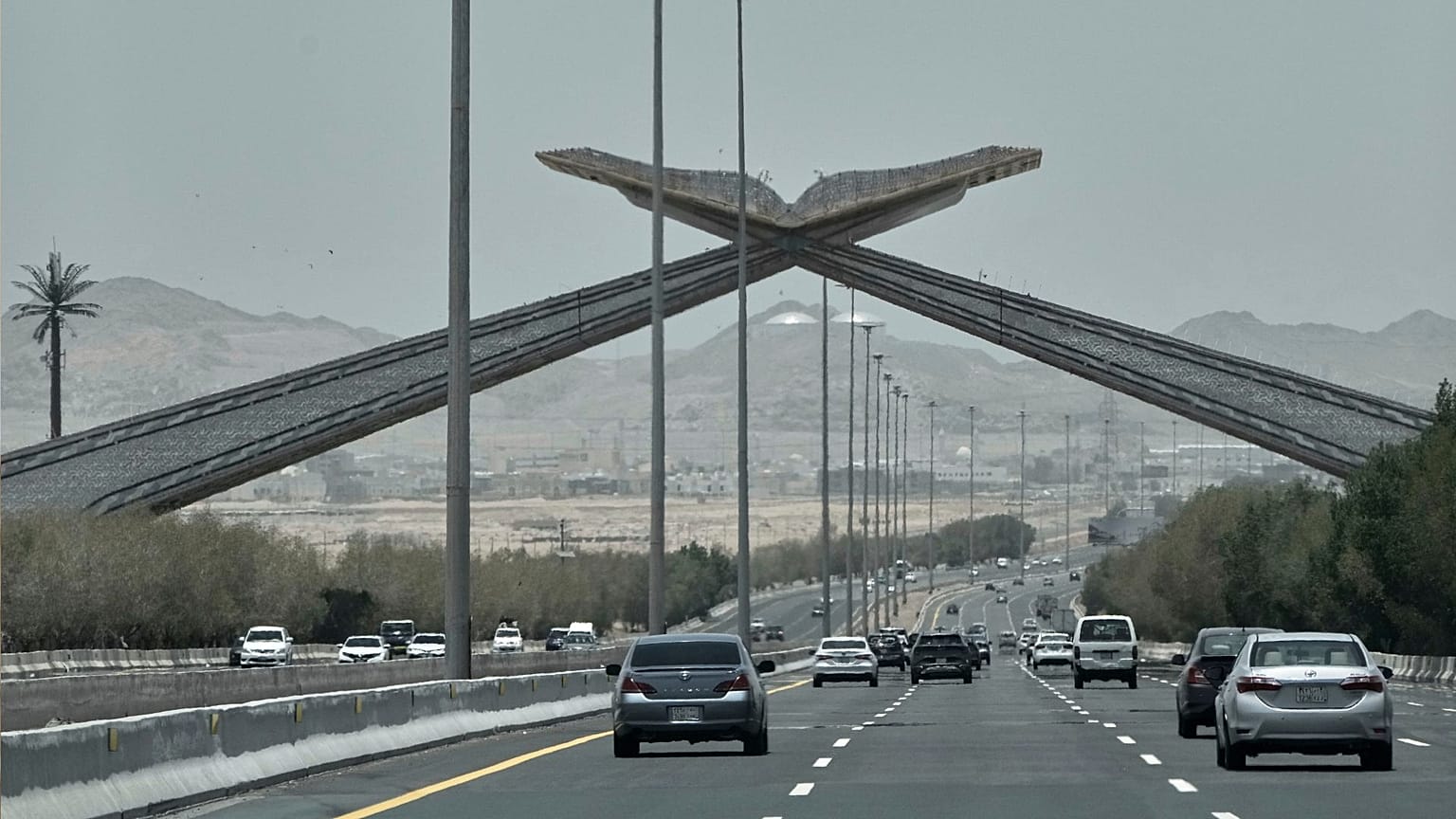 خودروها از زیر یک دروازه طاق‌مانند یادبود در بزرگراه جده ـ مکه، معروف به «دروازه قرآن»، عبور می‌کنند؛  ۲ ژوئن ۲۰۲۵