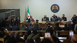 Des suspects se tiennent à l'intérieur d'une cellule de détention, à gauche, alors que des juges président le premier procès public de Syrie lié aux affrontements de mars, au Palais de justice d'Alep, 18 novembre 2025.