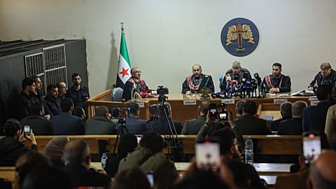 Des suspects se tiennent à l'intérieur d'une cellule de détention, à gauche, alors que des juges président le premier procès public de Syrie lié aux affrontements de mars, au Palais de justice d'Alep, 18 novembre 2025.
