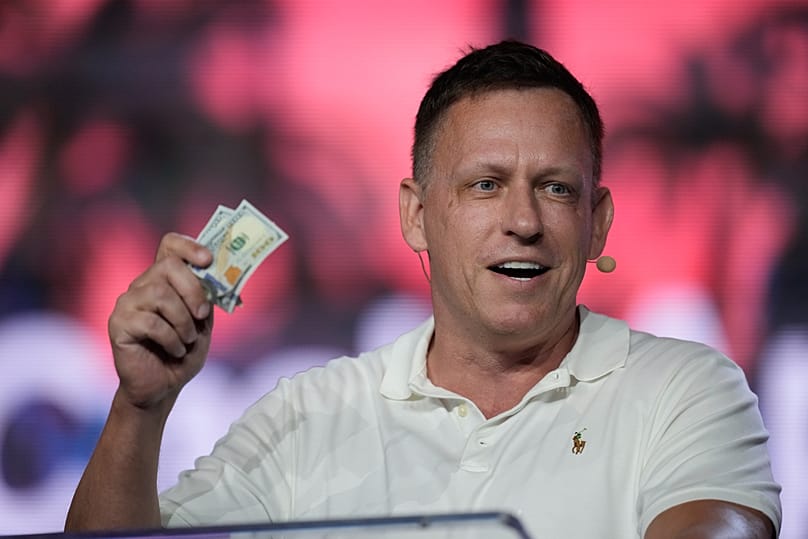 FILE - Peter Thiel, co-founder of PayPal and Palantir, offers a pair of hundred dollar bills to attendees during an address at the Bitcoin Conference in Florida. April 2022