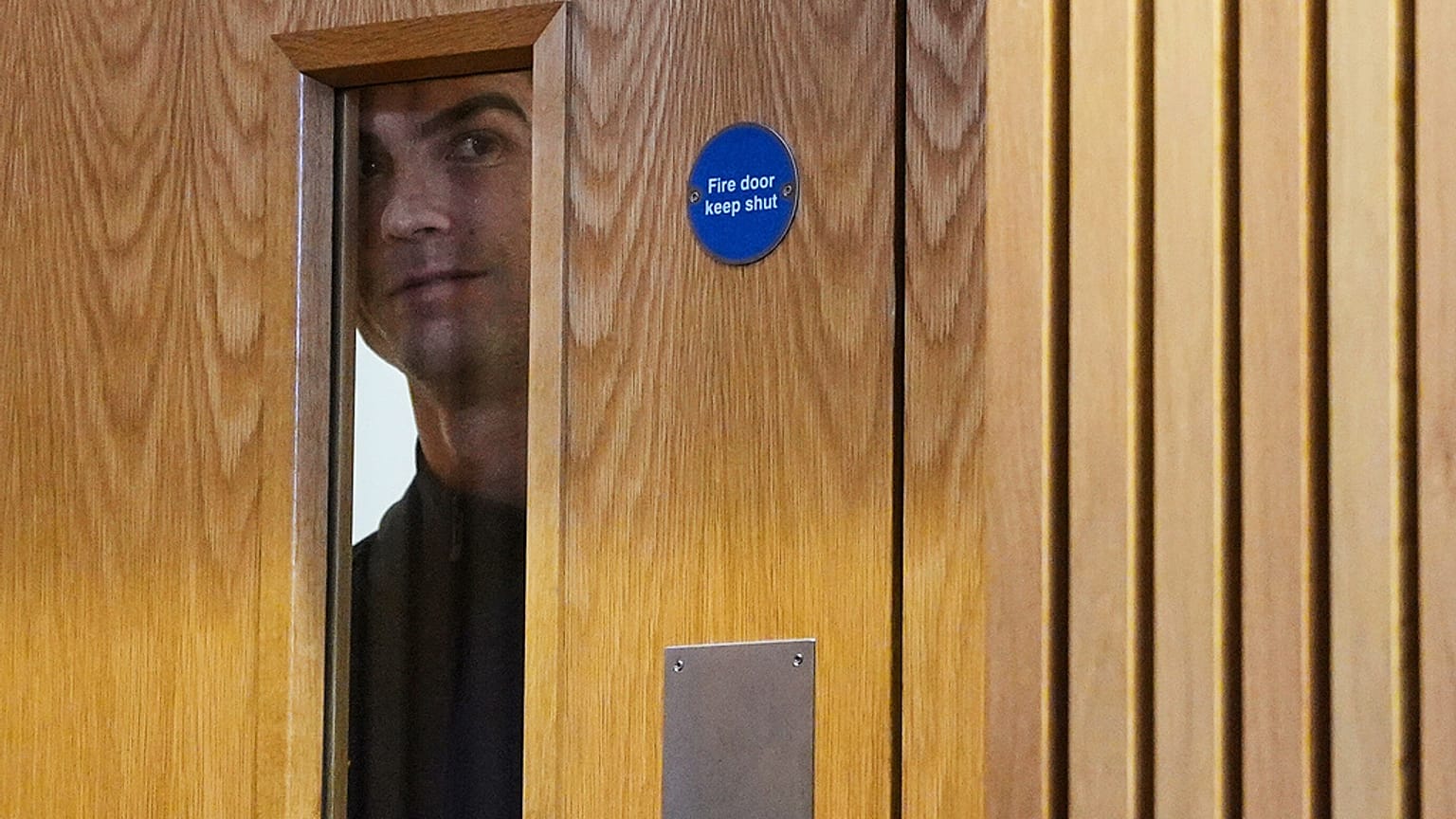 Cristiano Ronaldo espreita pela janela de uma porta durante uma conferência de imprensa em Dublin