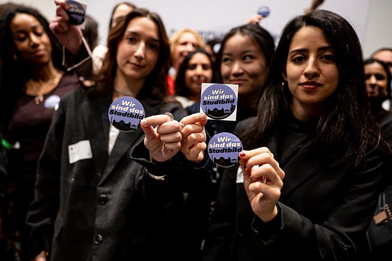 Stipendiatinnen halten Sticker hoch mit dem Aufdruck "Wir sind das Stadtbild" während der Rede von Bundeskanzler Friedrich Merz (CDU) in Berlin, 19. November 2025