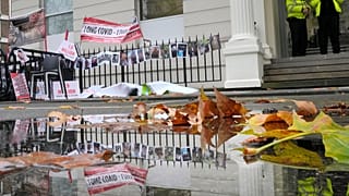 تنعكس لافتات وصور ضحايا كوفيد في بركة مياه خارج دورلاند هاوس أثناء إدلاء رئيس الوزراء البريطاني السابق بوريس جونسون بشهادته في التحقيق العام حول كوفيد-19 في لندن، 2023