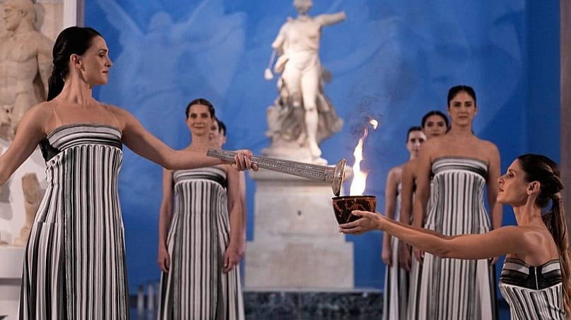High Priestess Mary Mina, left, lights a torch from the Olympic flame during the ceremony at the archaeological museum  of Olympia, 26 Nov 2025