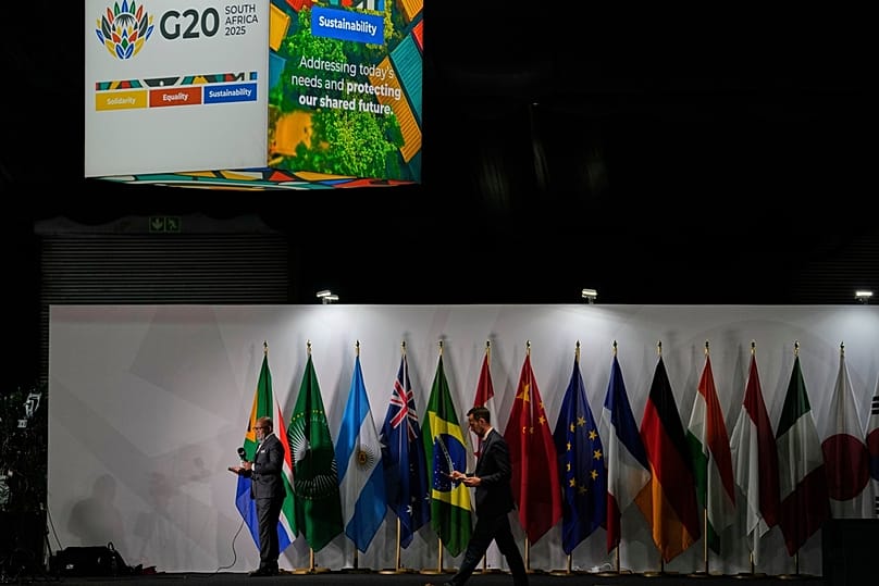  يقدم صحفي تقريره أثناء وقوفه بجانب أعلام الدول المشاركة في المركز الإعلامي لقمة مجموعة العشرين في جوهانسبرغ، جنوب أفريقيا، الجمعة 21 نوفمبر/تشرين الثاني 2025.