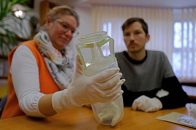 Hungarian archaeologists Gabriella Fenyes, left, and Gergely Kostyal inspect a glass flask found in an intact Roman sarcophagus, Wednesday, Nov. 19, 2025 in Budapest, Hungary.