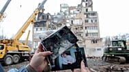 A woman looks on family photographs in front of a residential building which was heavily damaged by a Russian strike on Ternopil, Ukraine, Nov. 21, 2025