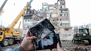 A woman looks on family photographs in front of a residential building which was heavily damaged by a Russian strike on Ternopil, Ukraine, Nov. 21, 2025