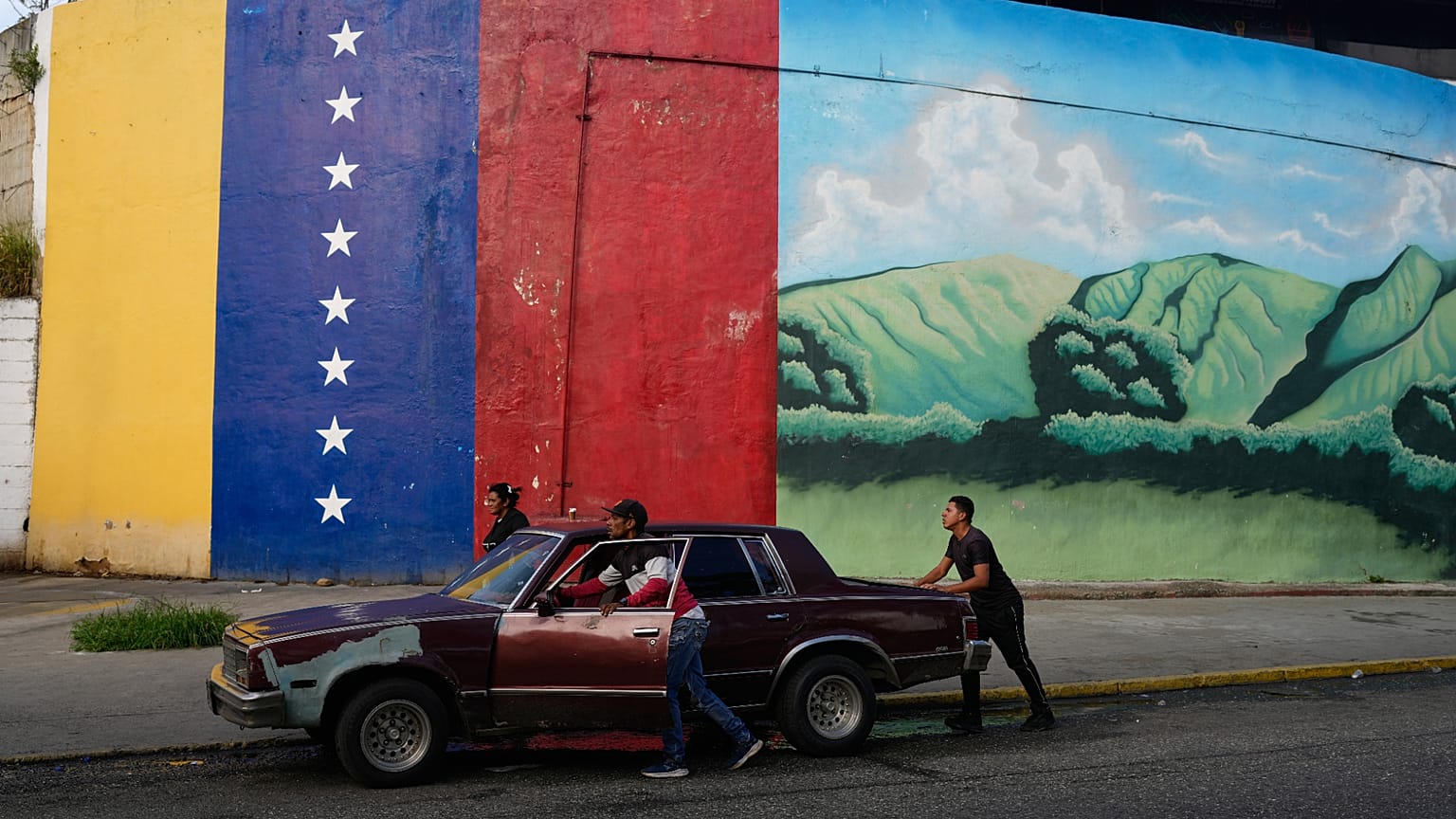 ARQUIVO: Pessoas empurram um carro parado em Caracas, 20 de novembro de 2025