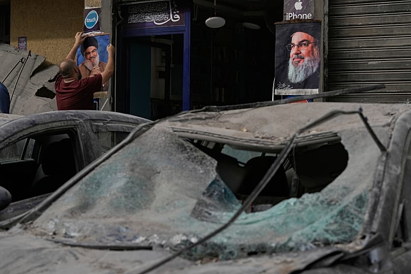 رجل يعلق ملصقًا لحسن نصر الله خارج متجر بينما تقف السيارات المدمرة في الشارع بعد الغارة  الإسرائيلية التي قتلت رئيس أركان حزب الله، يوم الاثنين 24 نوفمبر 2025