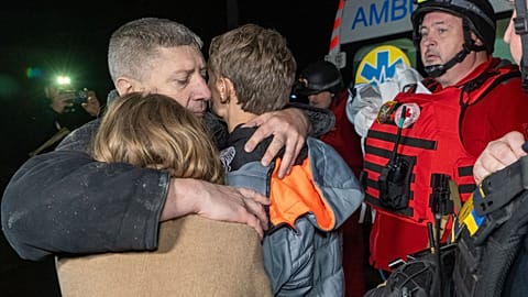 Un uomo abbraccia i suoi figli mentre piangono la morte della madre, uccisa in un attacco aereo russo.