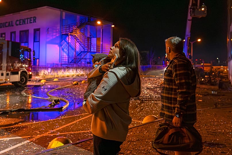 People watch as emergency services personnel work to extinguish a fire following a Russian attack in Kyiv, Ukraine, Tuesday, Nov. 25, 2025