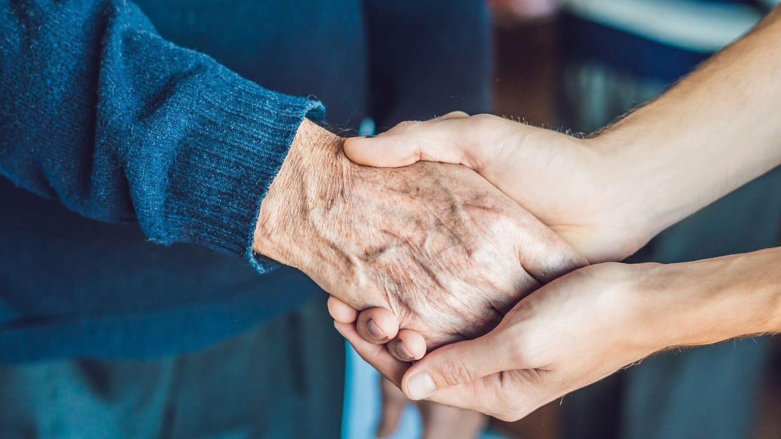 Eine Frau hält die Hand eines älteren Menschen.